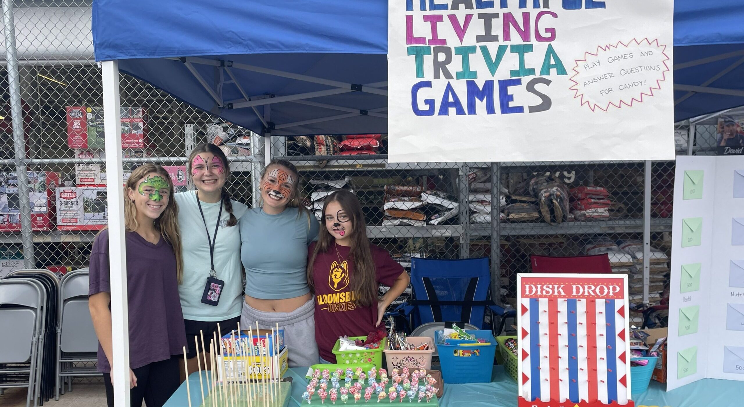 four students under a canopy in a sign that says Healthful Living Trivia Games at a community event