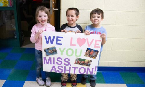 three prek students holding a sign for their teacher miss ashton saying we love you