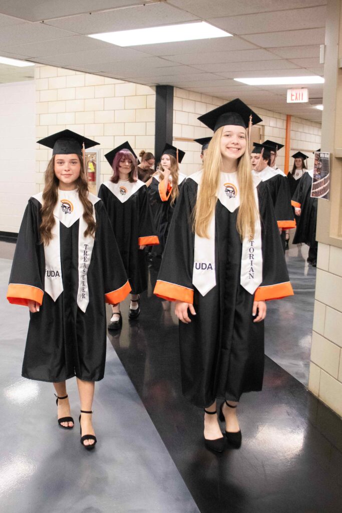 two girls in graduation gowns smiling in the school hallway